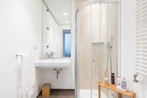 Une salle de bain moderne avec une douche à parois de verre, un lavabo avec des articles de toilette et un meuble-lavabo en bois.