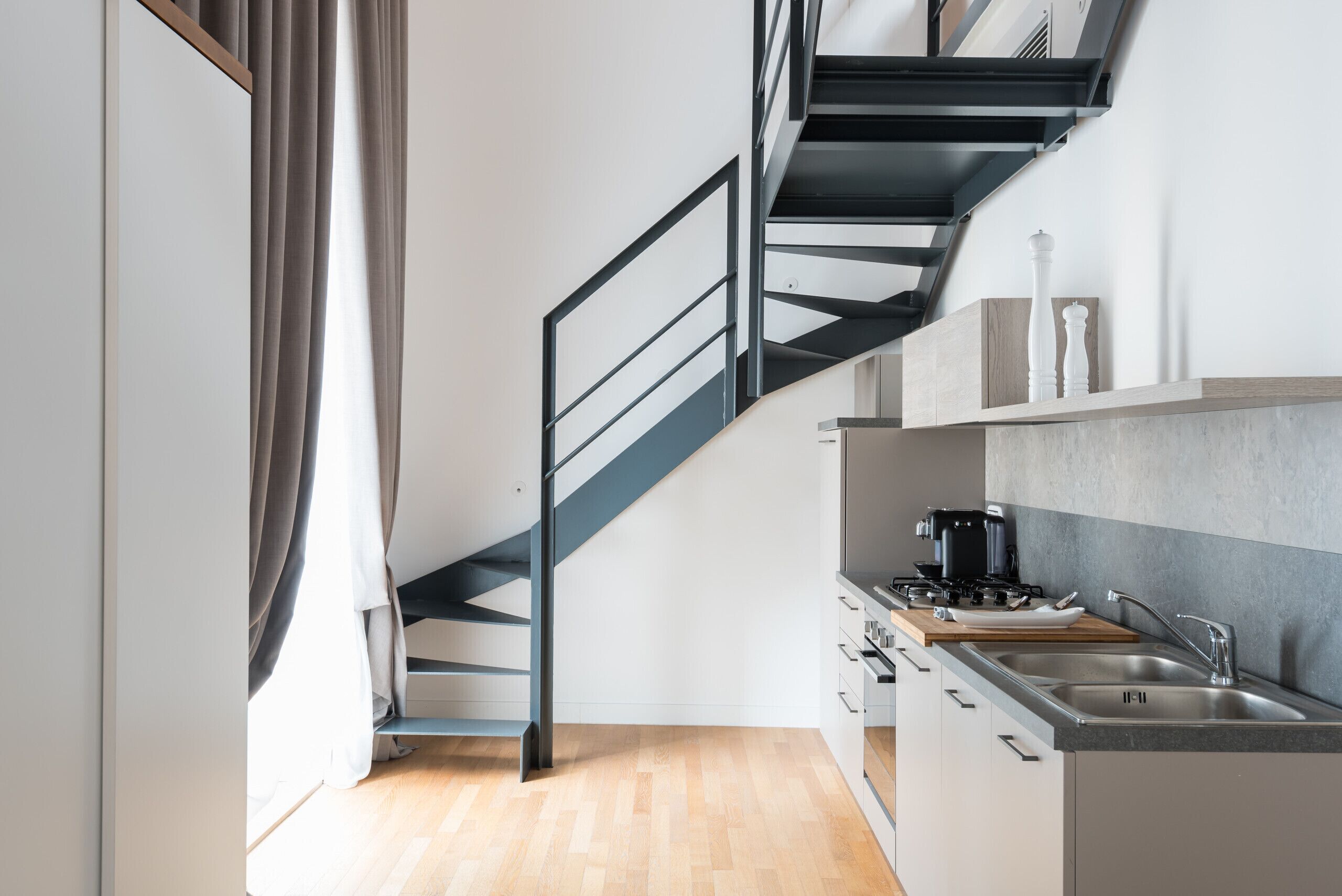 A modern kitchen with a built-in stove, a sink, and a staircase leading to an upper level.
