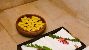 A bathroom with a wooden bowl of yellow flowers, two white towels with pink flowers, and towels hanging on the wall.