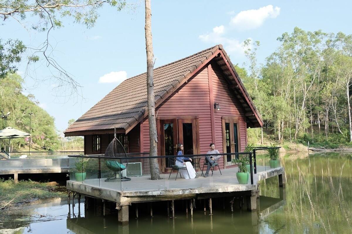 A wooden cabin with a red roof on stilts over water, surrounded by trees.