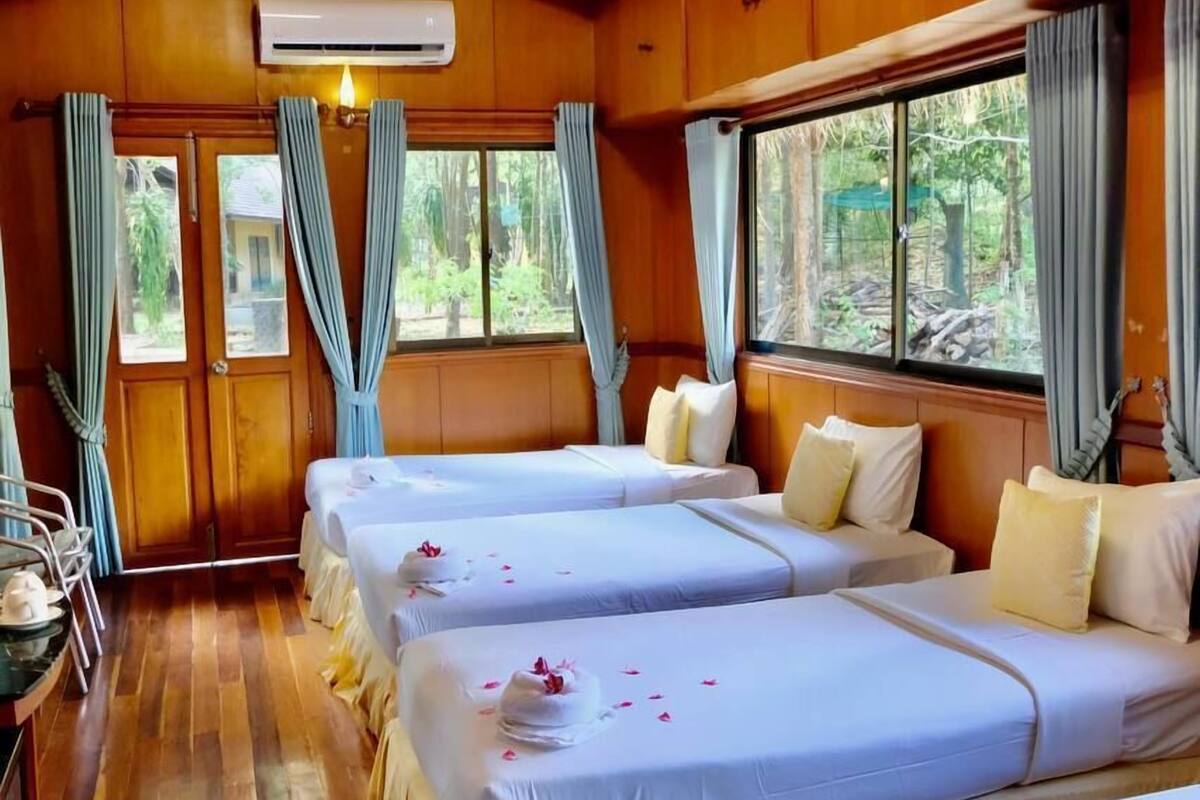 A room with two beds, wooden walls, a window, and an air conditioning unit.