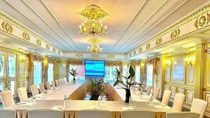 Un comedor formal con una larga mesa dispuesta para un banquete, rodeada de sillas, un candelabro y molduras decorativas en las paredes.