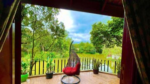 Una terraza de madera con una hamaca colgante y plantas en macetas, con vistas a un estanque y abundante vegetación.