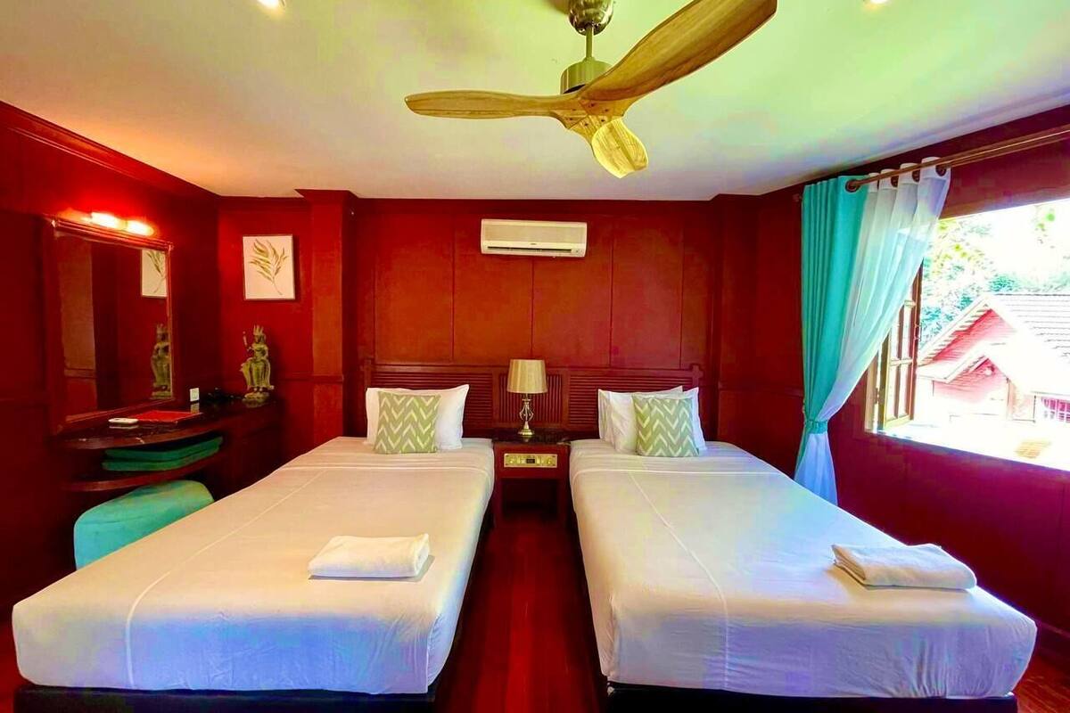 A hotel room with two beds, a ceiling fan, a nightstand, a lamp, and a window with curtains.