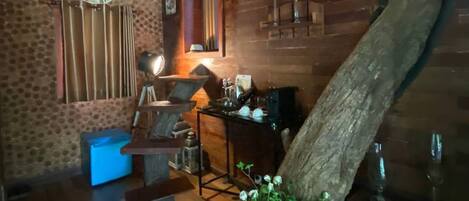 Interior rústico com paredes de madeira, uma grande viga de madeira, um relógio e uma planta.