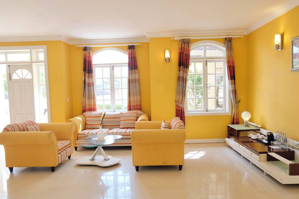 A bright living room with yellow walls, a sofa set, a coffee table, and a side table with a lamp.