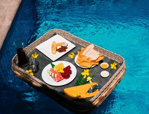 A dining setup by a pool with a wicker tray containing food, drinks, and utensils. - Kirirom Hillside Resort (Phnom Sruoch)