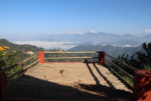 Uma plataforma de madeira com corrimão, com vista para uma paisagem montanhosa sob um céu claro.