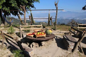 Ambiente rústico ao ar livre com redes, cerca de madeira e uma mesa com cestos de fruta.