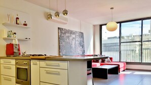 A modern kitchen with white cabinets, a built-in oven, and a red appliance. There is a large window with a view of the city. - Hilton Beach Stunning Designer 2BR APT (Tel Aviv)