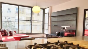 A modern kitchen with a gas stove, large windows, and a red sofa. - Hilton Beach Stunning Designer 2BR APT (Tel Aviv)