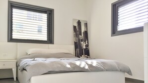 A bedroom with a bed, nightstands, and a cityscape artwork on the wall. - Hilton Beach Stunning Designer 2BR APT (Tel Aviv)