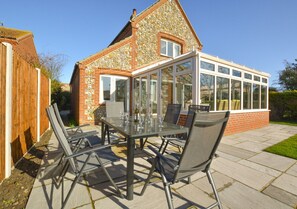 Enjoy a serene view of the garden from the adjacent conservatory, featuring a glass-top table and comfortable seating for four.