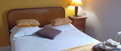 Una cama bien hecha con ropa de cama blanca y marrón, una lámpara de noche y una toalla doblada sobre una mesita de noche.