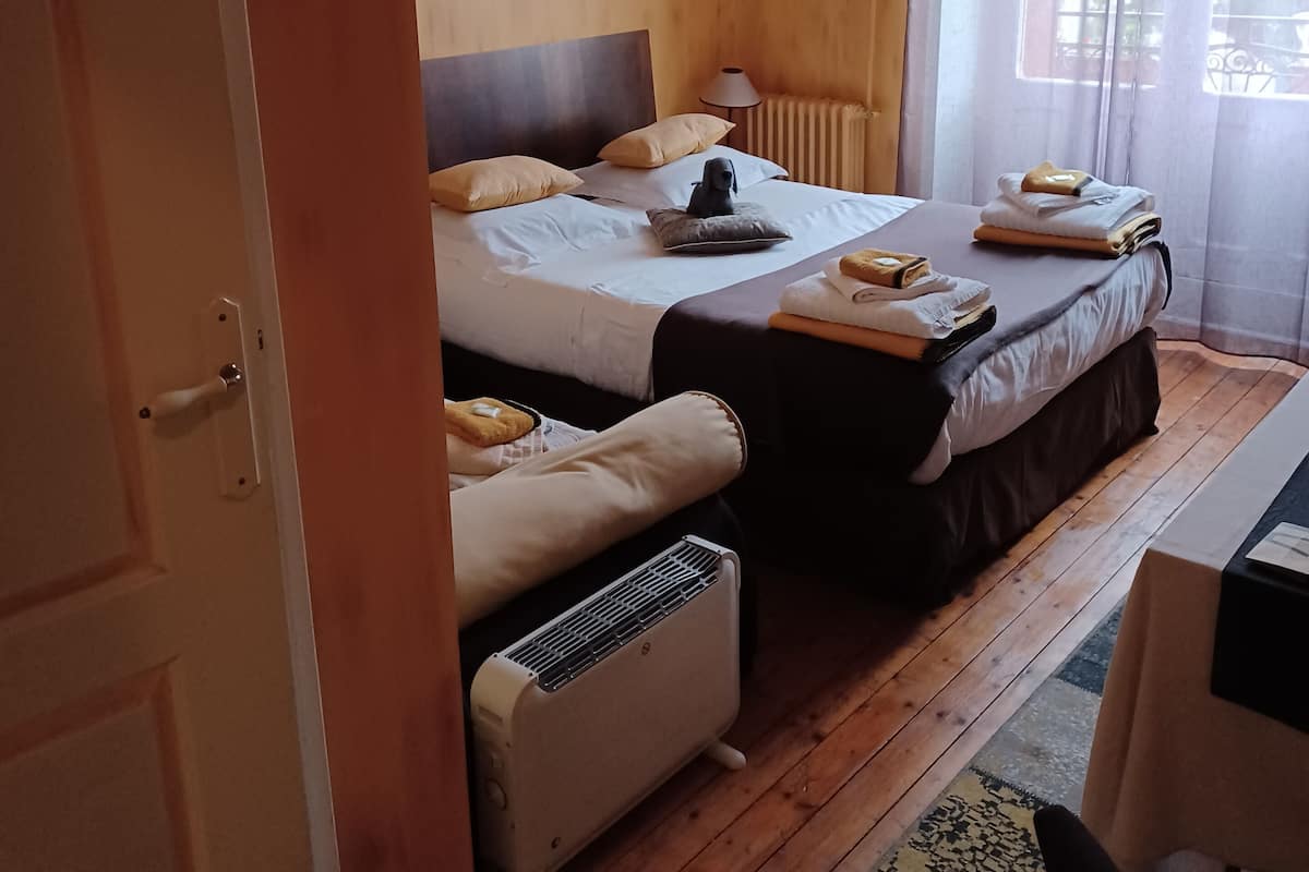 A hotel room with two beds, a heater, a window with curtains, and a small table with towels.