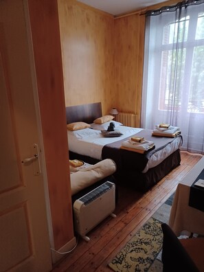 A hotel room with two beds, a heater, a window with curtains, and a small table with towels. - Hôtellerie Les Lilas (Bourgueil)