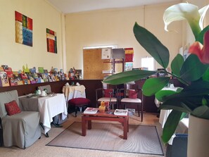 A cozy hotel room with a dining area, a small table with a red cushion, and a large green plant in the foreground. - Hôtellerie Les Lilas (Bourgueil)