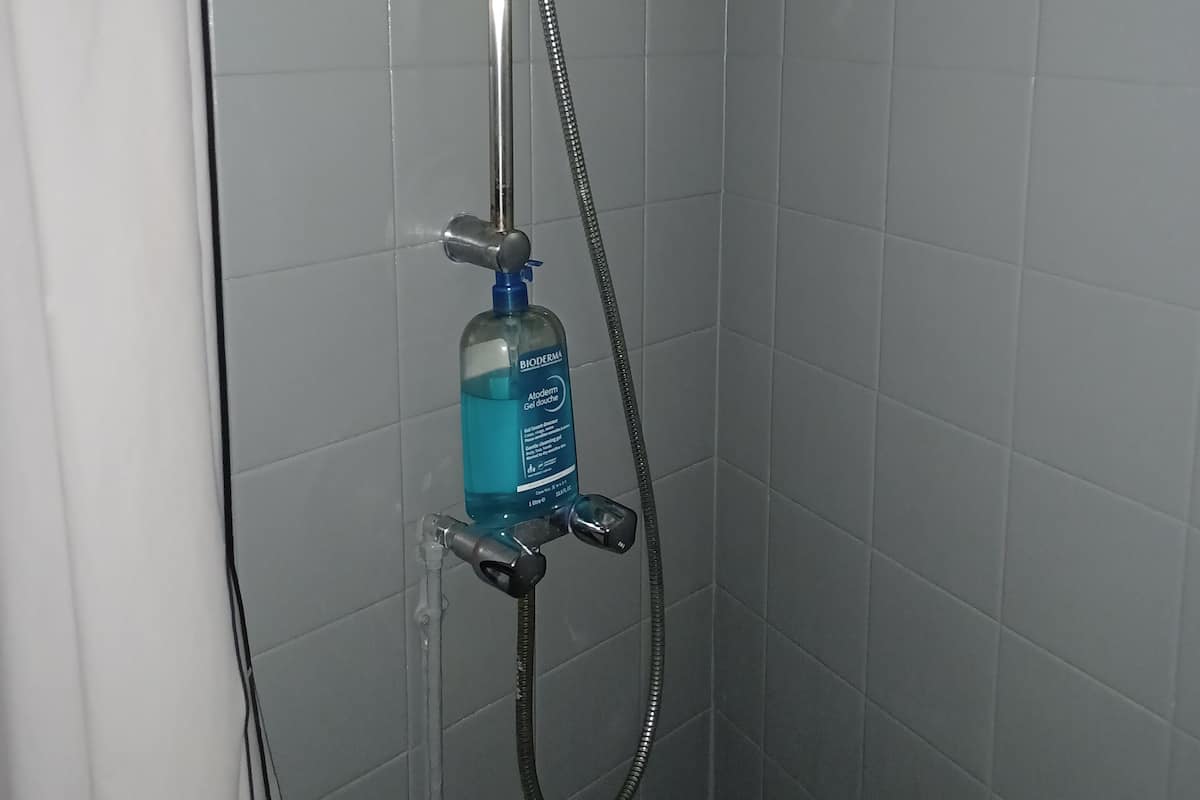 A shower with a handheld showerhead and a bottle of Bioderma Aloe Gel douche.
