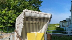 A wicker chair with a striped cushion and a yellow pillow, positioned on a wooden deck with a railing. - Traumsegler, Germany (Breege)