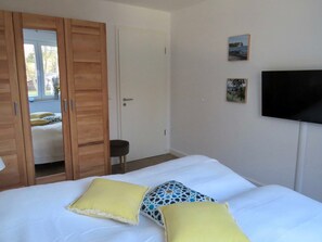 A bedroom with a bed, a wooden wardrobe, a television on the wall, and a door leading to another room.