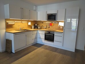 A modern kitchen with white cabinets, a built-in oven, a microwave, a sink, and a coffee maker.