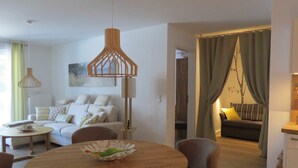 A modern living room with a sofa, a dining table, and a kitchen area visible through an open doorway. - Traumsegler, Germany (Breege)