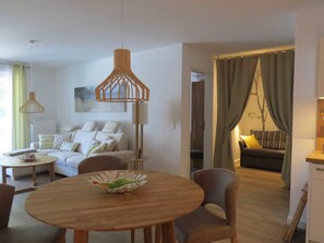 A modern living room with a sofa, a dining table, and a kitchen area visible through an open doorway.