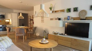 A modern living room with a sofa, dining table, chairs, a TV, and a kitchen area. - Traumsegler, Germany (Breege)