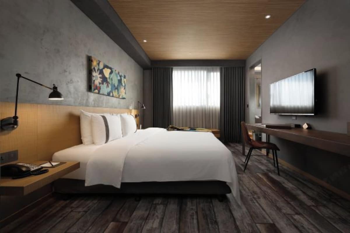 A modern hotel room with a large bed, a desk, a flat-screen TV, and a painting on the wall.