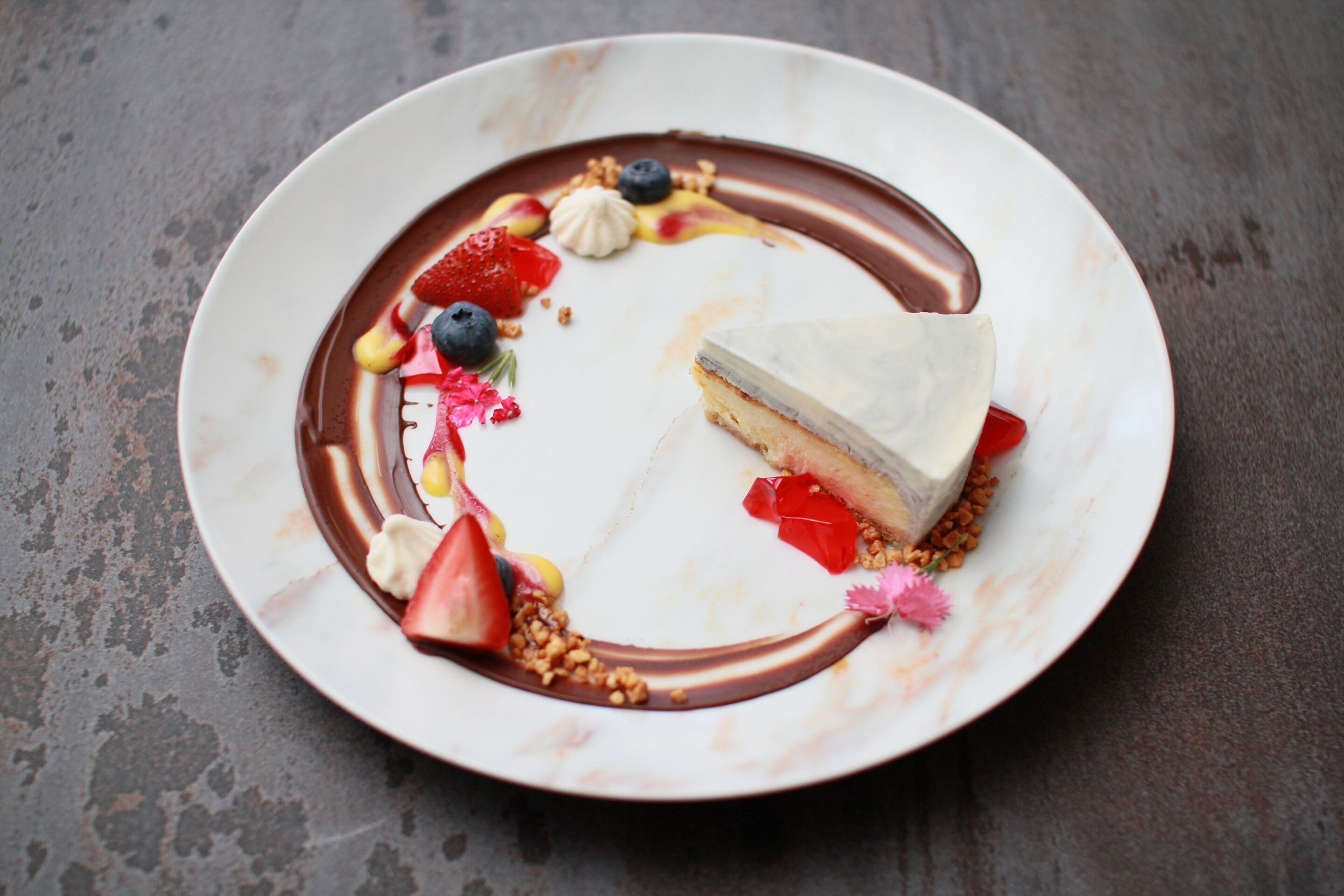 A dessert plate with a slice of cake, strawberries, blueberries, and chocolate sauce.