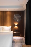 Camera d'albergo moderna con parete rivestita in legno, una lampada da parete decorativa, un letto con lenzuola bianche e un comodino.