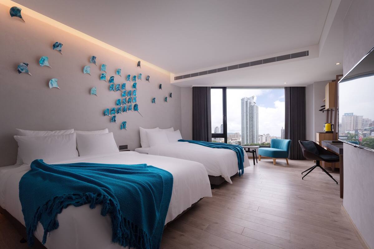 A modern hotel room with two beds, a city view, and a unique wall art installation.