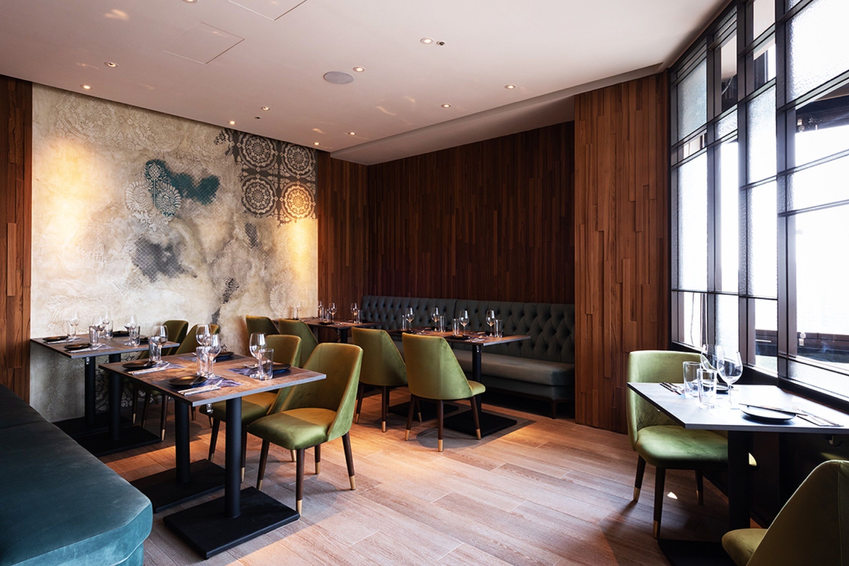 A restaurant with wooden panel walls, green upholstered chairs, and tables set for dining.
