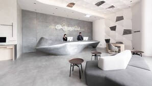 A modern reception area with a unique wave-shaped desk, a large wall art piece, and a seating area with a sofa and small tables. - Brio Hotel (Kaohsiung)