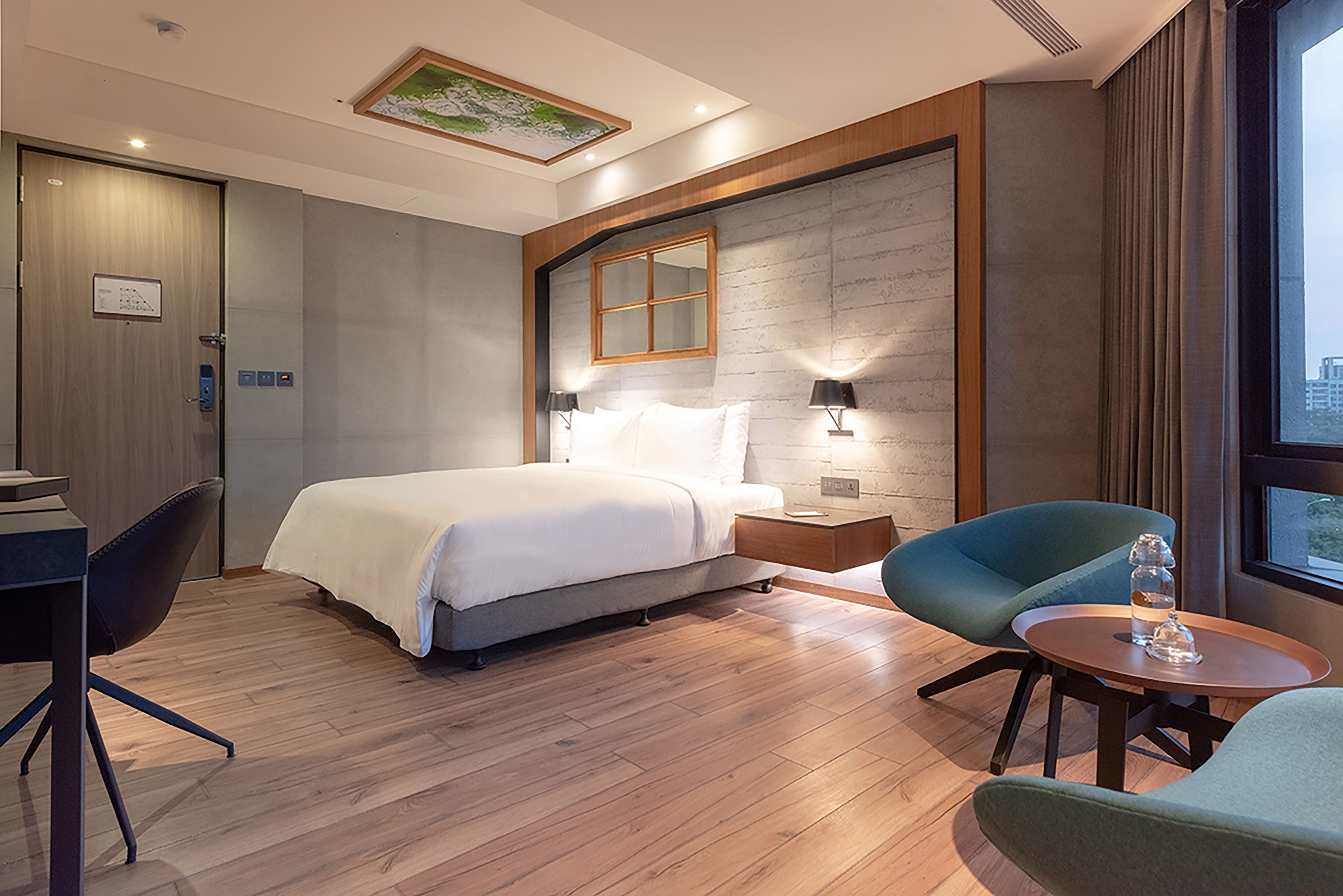 Habitación de hotel con una cama, un escritorio, dos sillas, una mesita y una ventana con cortinas.