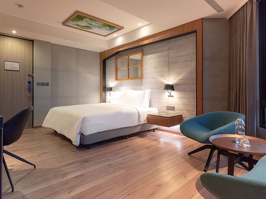 A hotel room with a bed, a desk, two chairs, a small table, and a window with curtains.