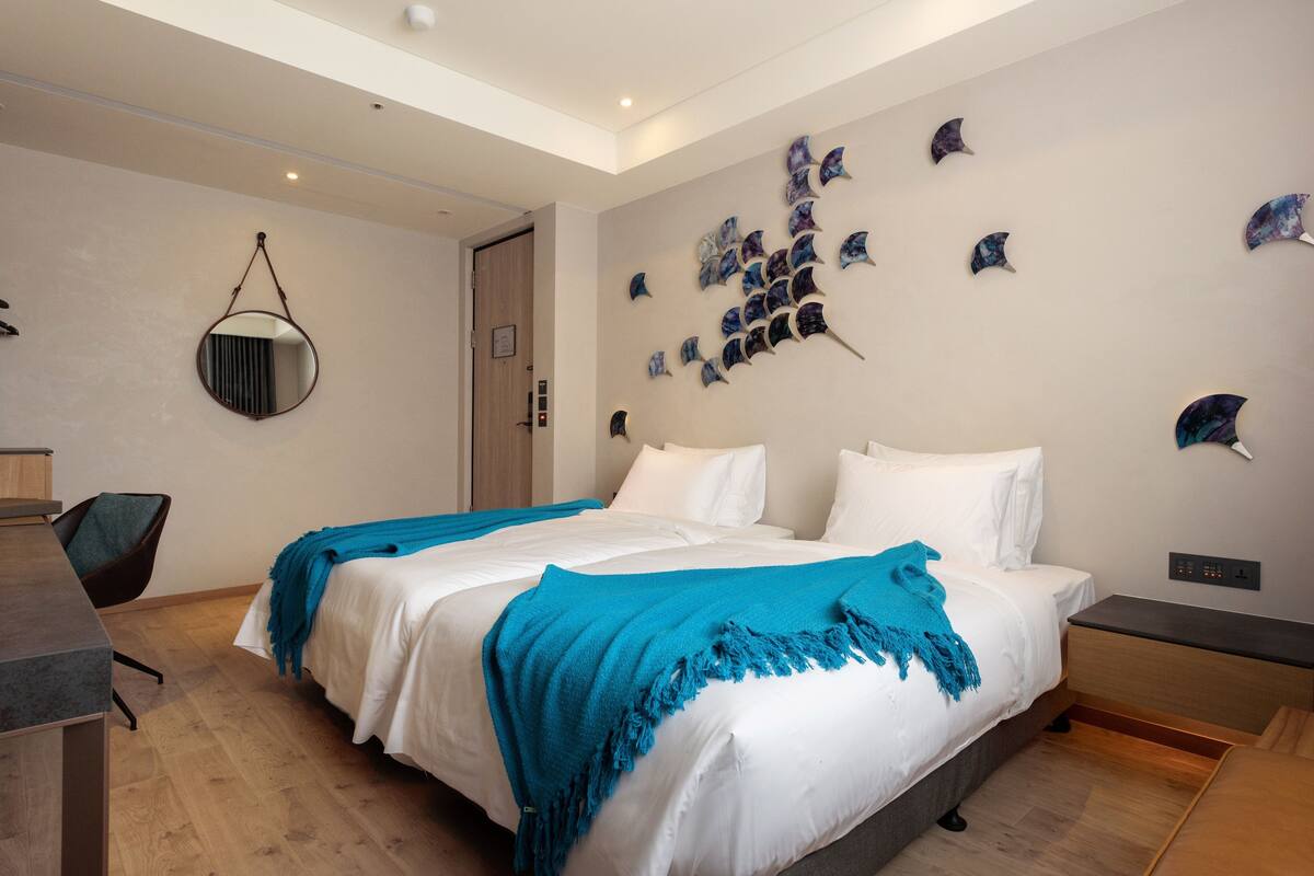 A modern bedroom with a large bed, a desk, and a wall-mounted mirror.