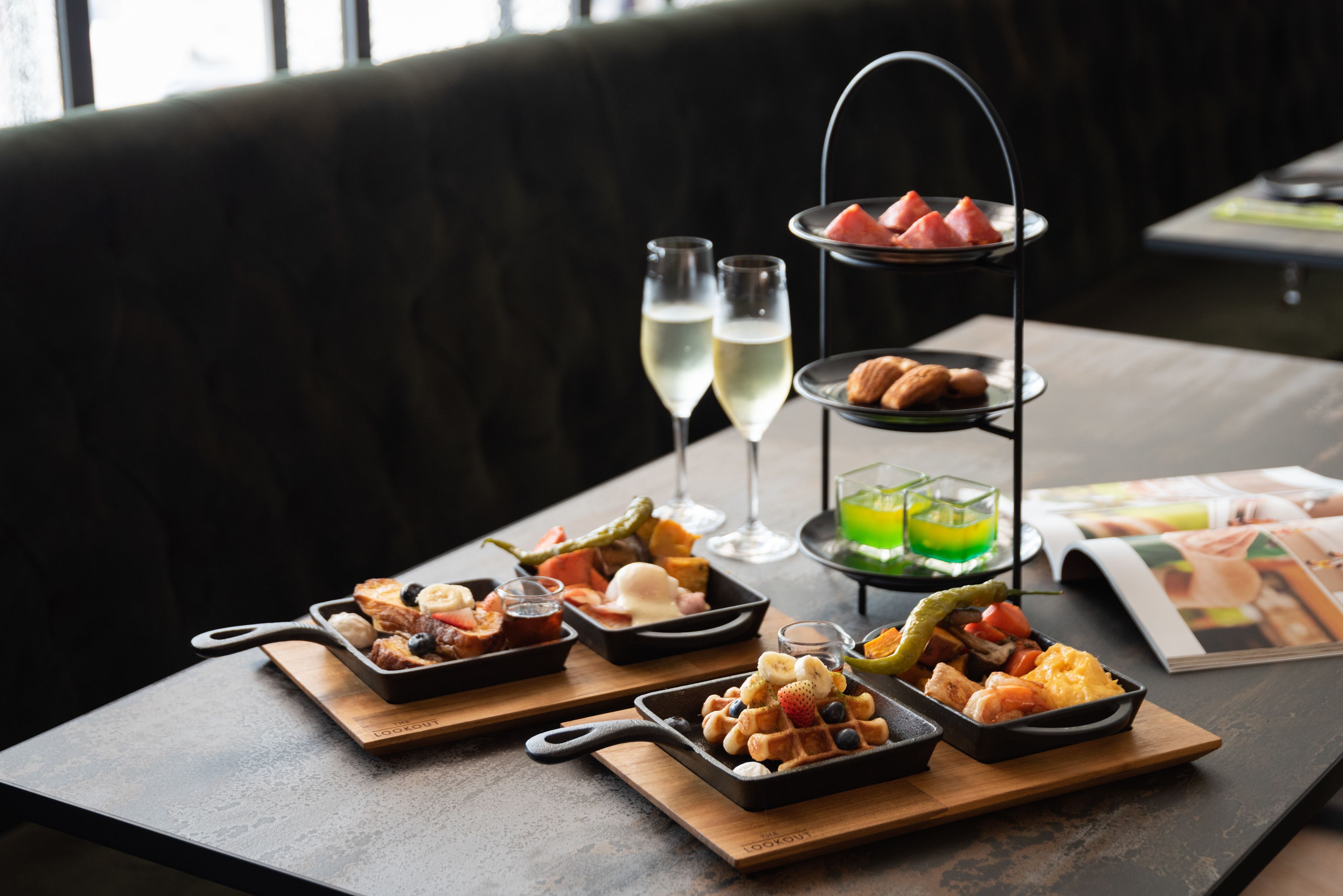 Une table à manger dressée avec divers aliments pour le petit-déjeuner, notamment des gaufres, des fruits et des viennoiseries, accompagnée de deux verres de vin blanc.