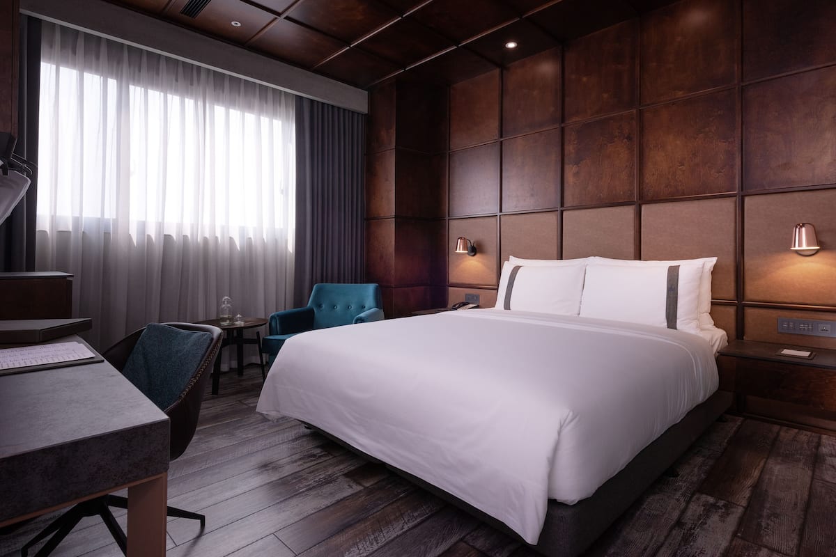 A modern hotel room with a large bed, a desk, a chair, and a small table.