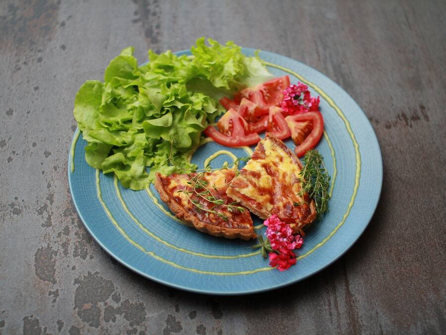 A plate with a slice of quiche, lettuce, and tomato slices on a blue plate.