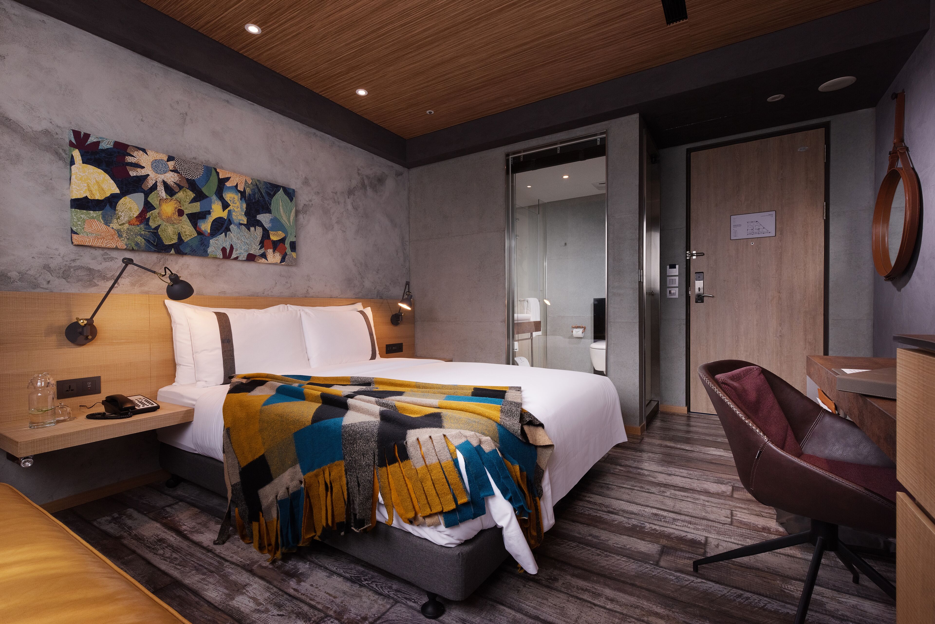 A modern hotel room with a large bed, a desk, a chair, and a wooden ceiling.