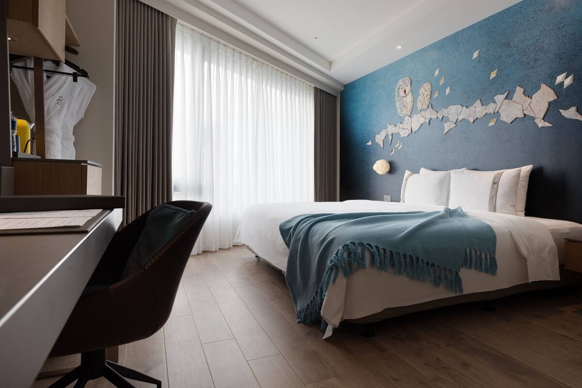 A modern hotel room with a bed, a desk, and a chair.