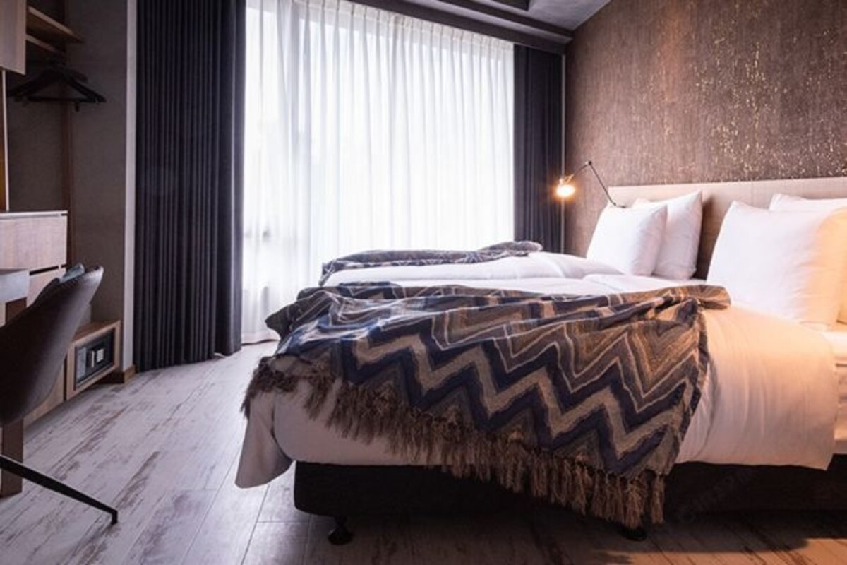 Una habitación de hotel moderna con cama, escritorio y un ventanal con cortinas.