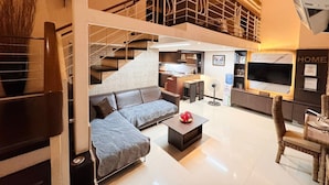 A modern living room with a sectional sofa, a coffee table, and a dining area with wicker chairs. - Super Cebu Loft (Cebu City)