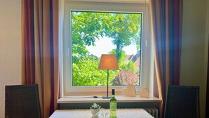 Ett rum med ett bord dukat för två personer, ett fönster med gardiner, en lampa och en flaska på fönsterbrädan.