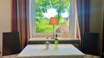 Et værelse med et bord dækket til to personer, et vindue med gardiner, en lampe og en flaske på vindueskarmen.