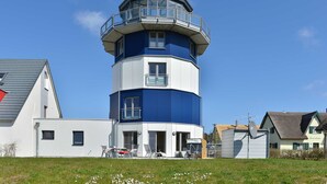 A multi-story lighthouse with a blue and white exterior, a balcony on the upper floor, and a small satellite dish on the side.