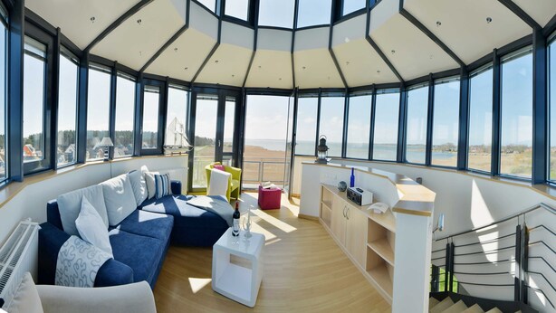 A modern interior with a large windowed area, a blue sofa, a white coffee table, and a kitchen area.
