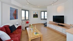 A modern living room with a red sofa, a wooden coffee table, a TV, and artwork on the walls.