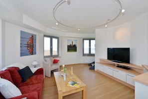 A modern living room with a red sofa, a wooden coffee table, a TV, and artwork on the walls.